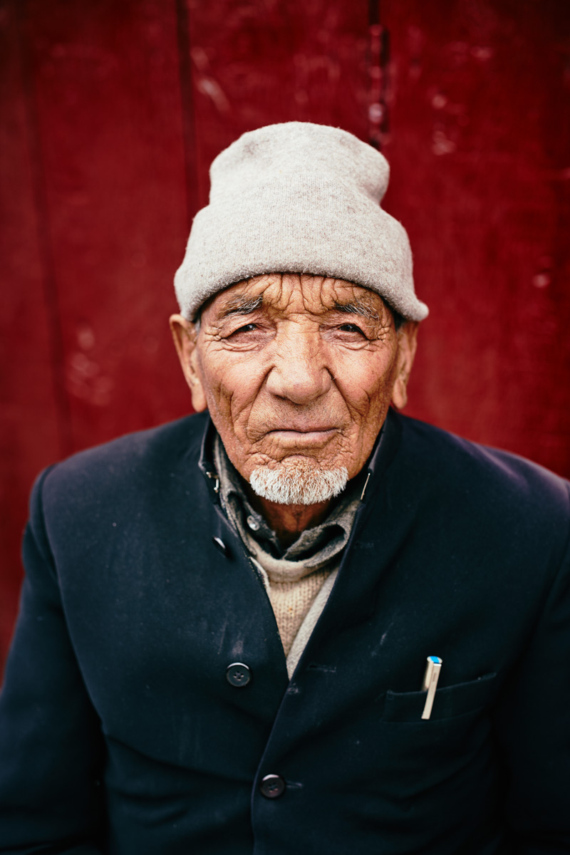Portrait von altem Mann mit Mütze vor rotem Hintergrund in Kargil/ Ladakh/ Indien, 2018