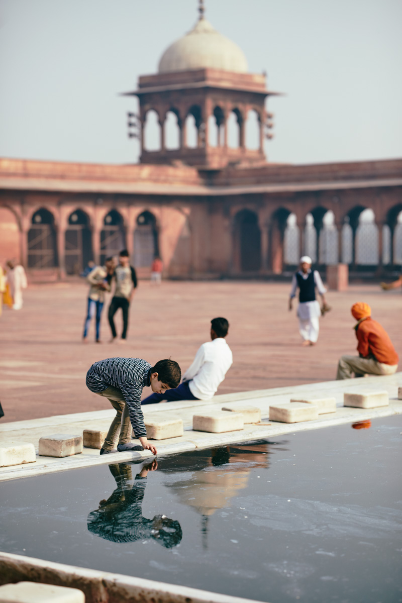 Junge der sich im Wasser spiegelt, an der Jama Masjid Moschee in Delhi/ Indien, 2018